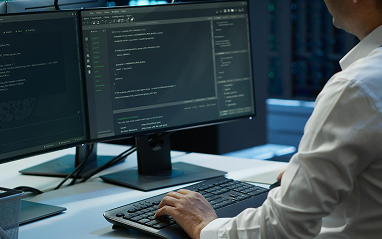 A man focused on his work, using two computer screens to manage tasks and information simultaneously.
